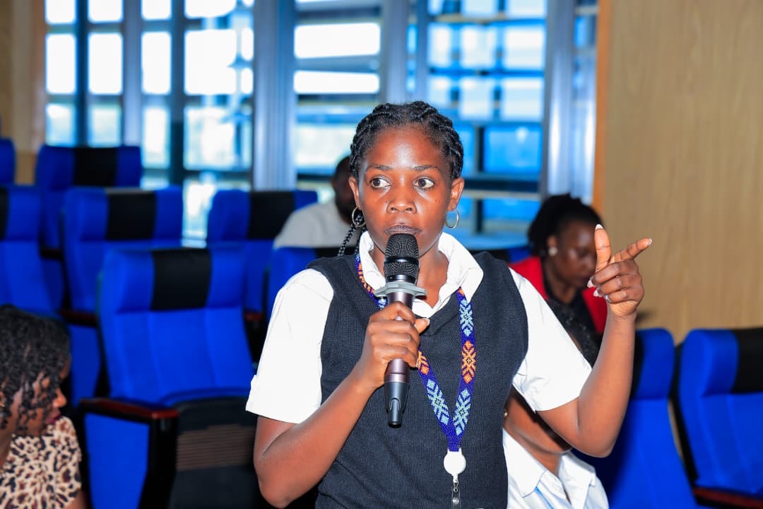 A woman in the audience stands with a microphone, asking a question during the relaunch, in a blue auditorium.