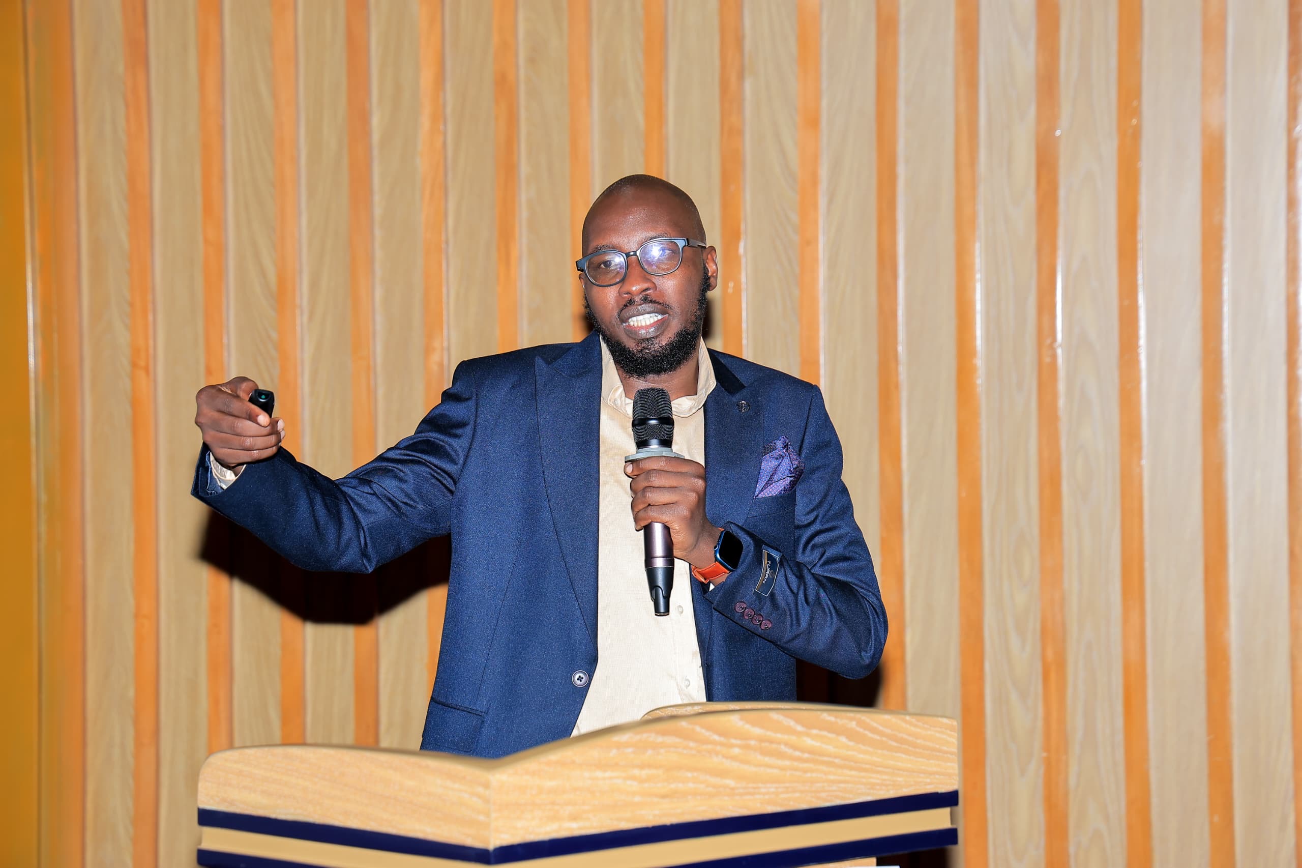 Michael Cengkuru presenting at the GPP relaunch, holding a presentation clicker and microphone, mid-gesture.