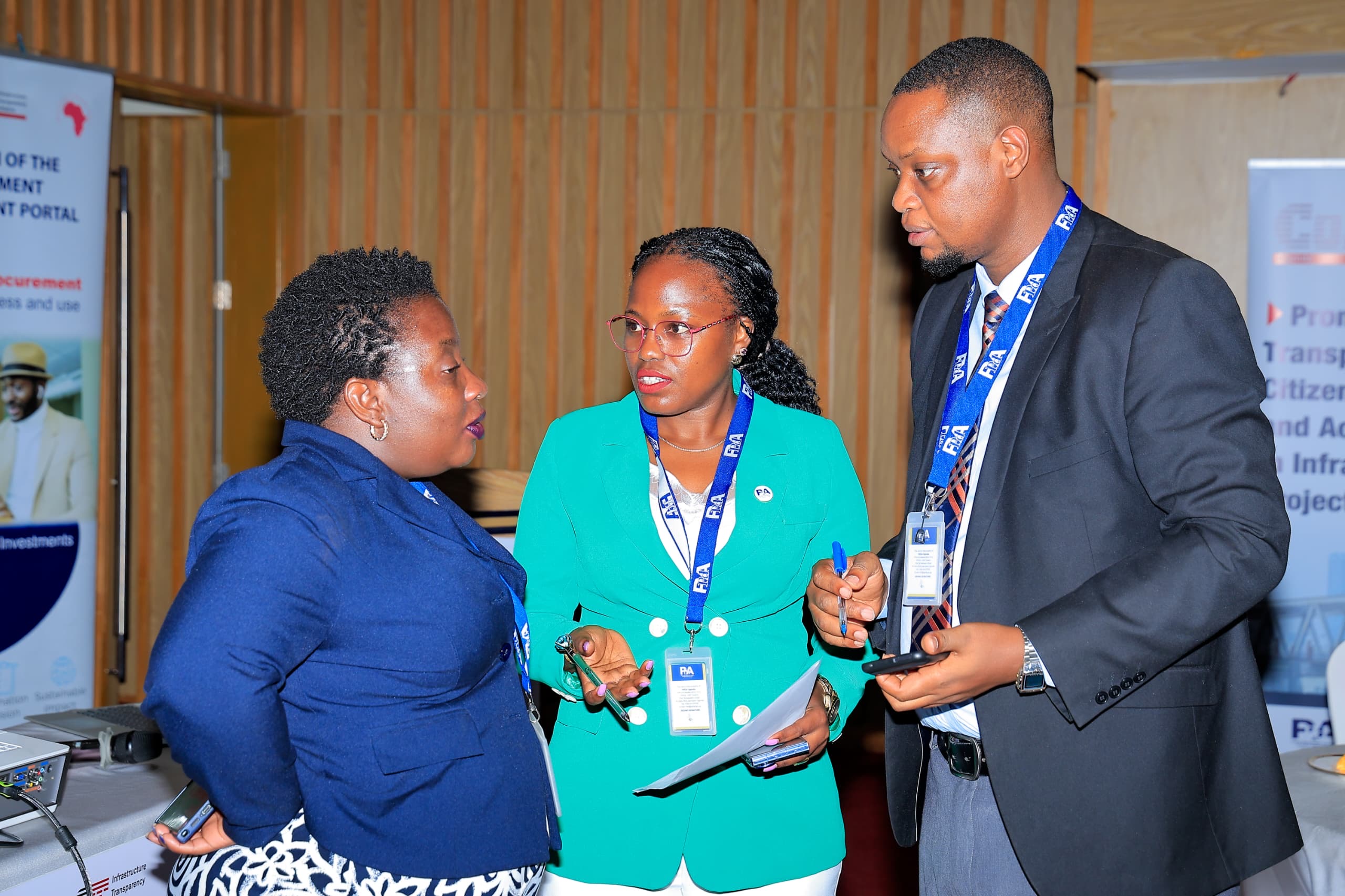 Three people in a candid side conversation after the event, one holding a phone, beside a portal banner.