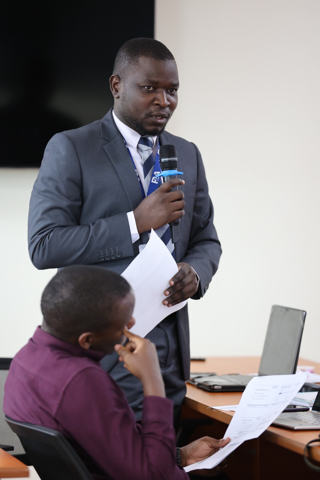 A procurement officer stands with a microphone to put a question to the room during the Kampala training